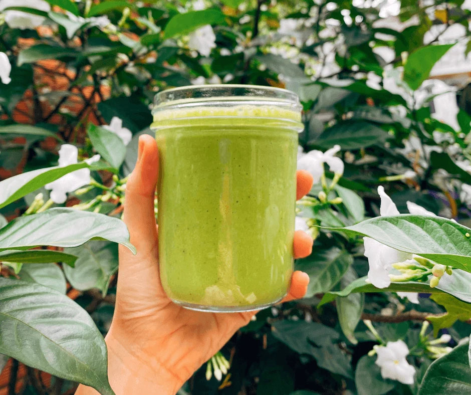 Bright Summer Green Smoothie with Mango & Coconut in a jar held against a lush, tropical background.