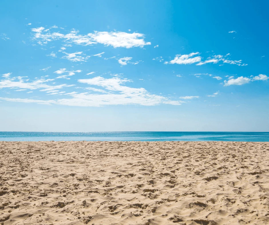 Summer Wellness Habits: Align Your Routine with the Season beach scene with sandy shore and clear blue sky.