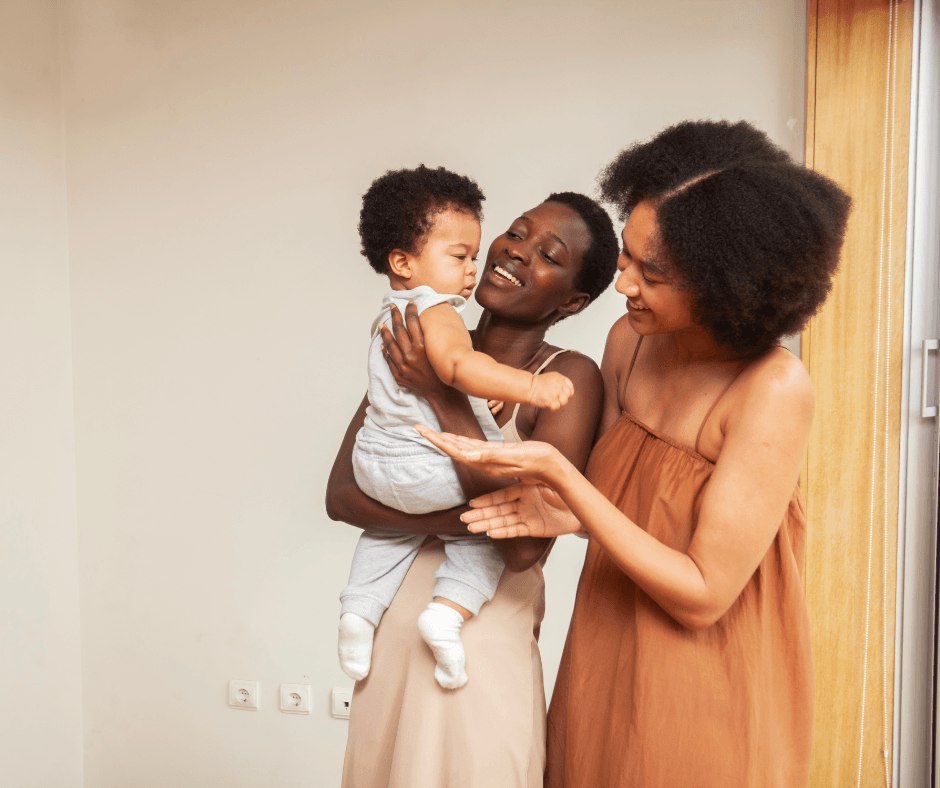 two women holding a baby and smiling