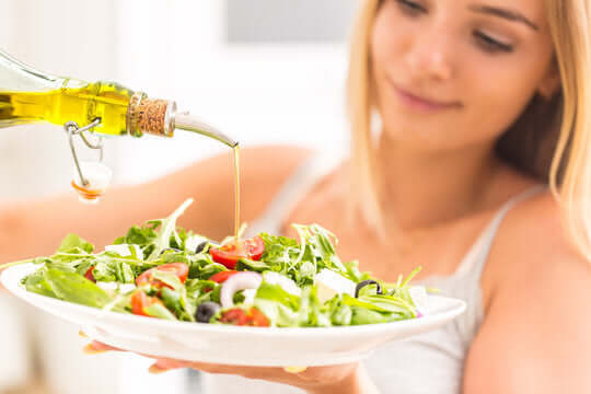 a woman eating a salad while drizzling flax oil on top of it