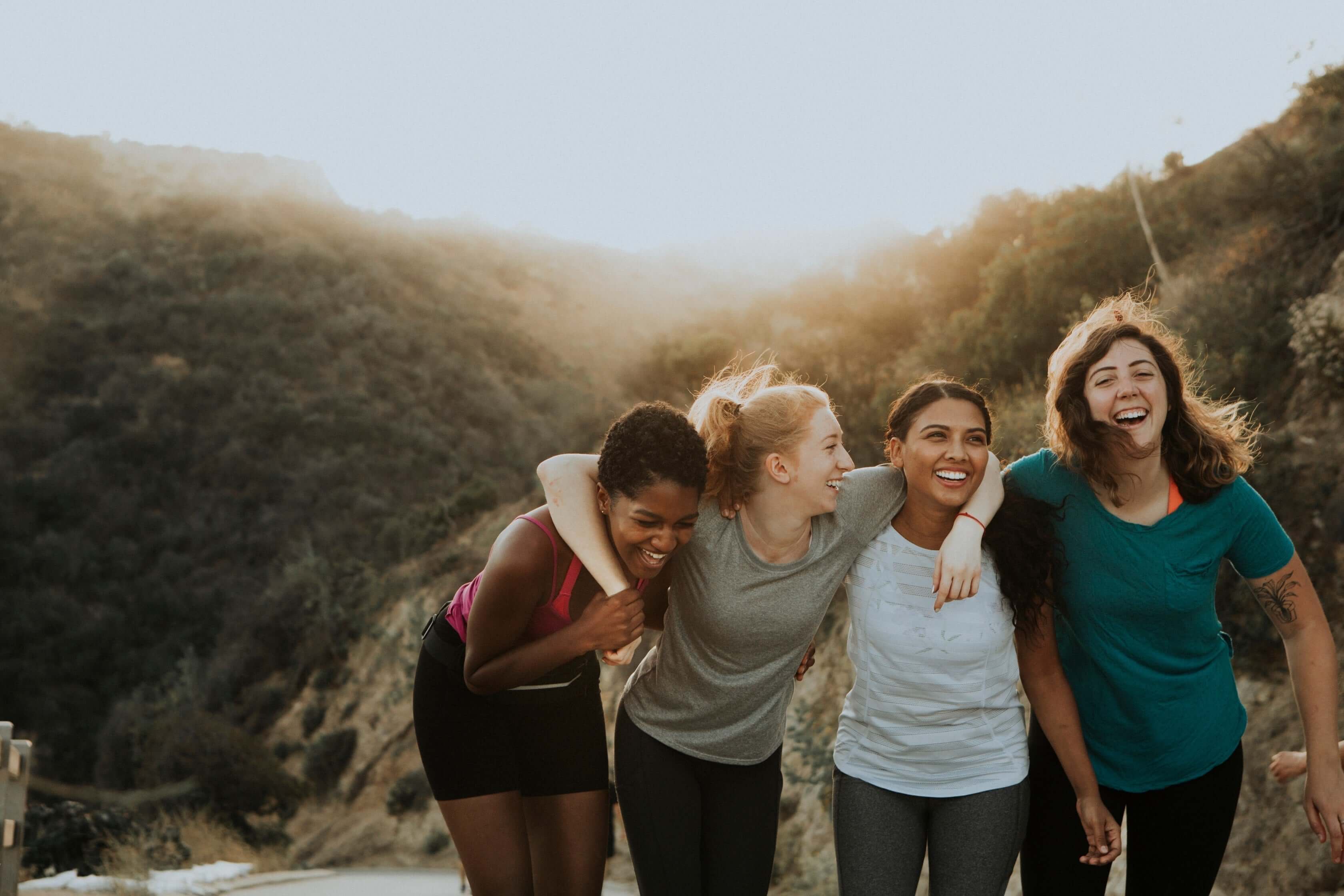 four women smiling and embracing outside on a trail