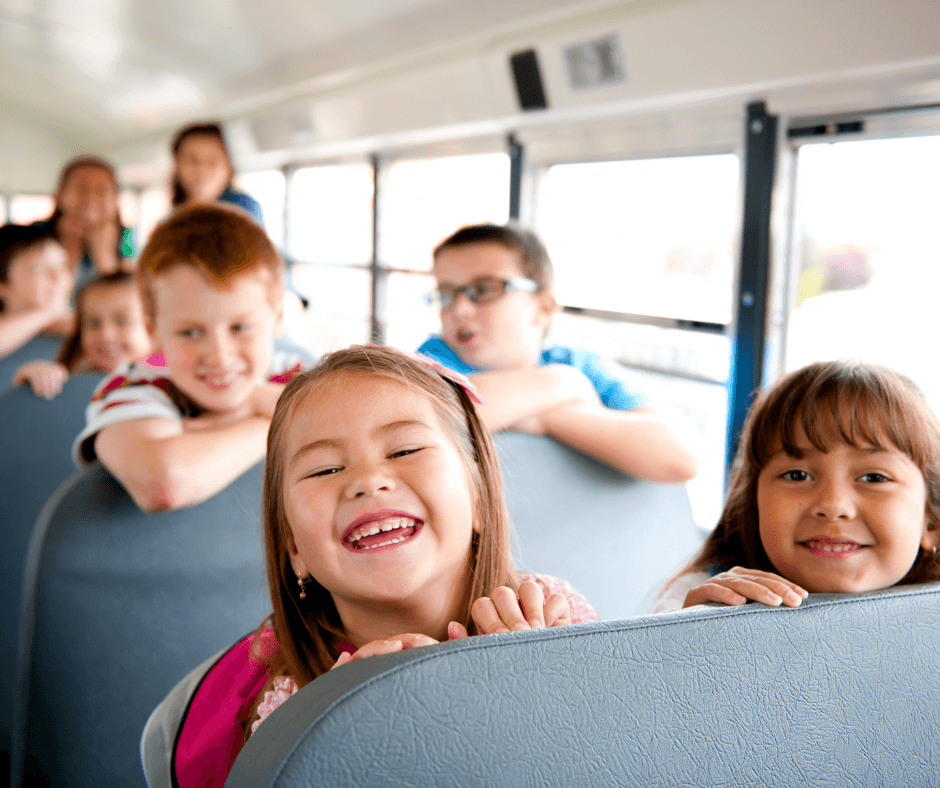 rows of smiling kids on a school bus with two girls up front