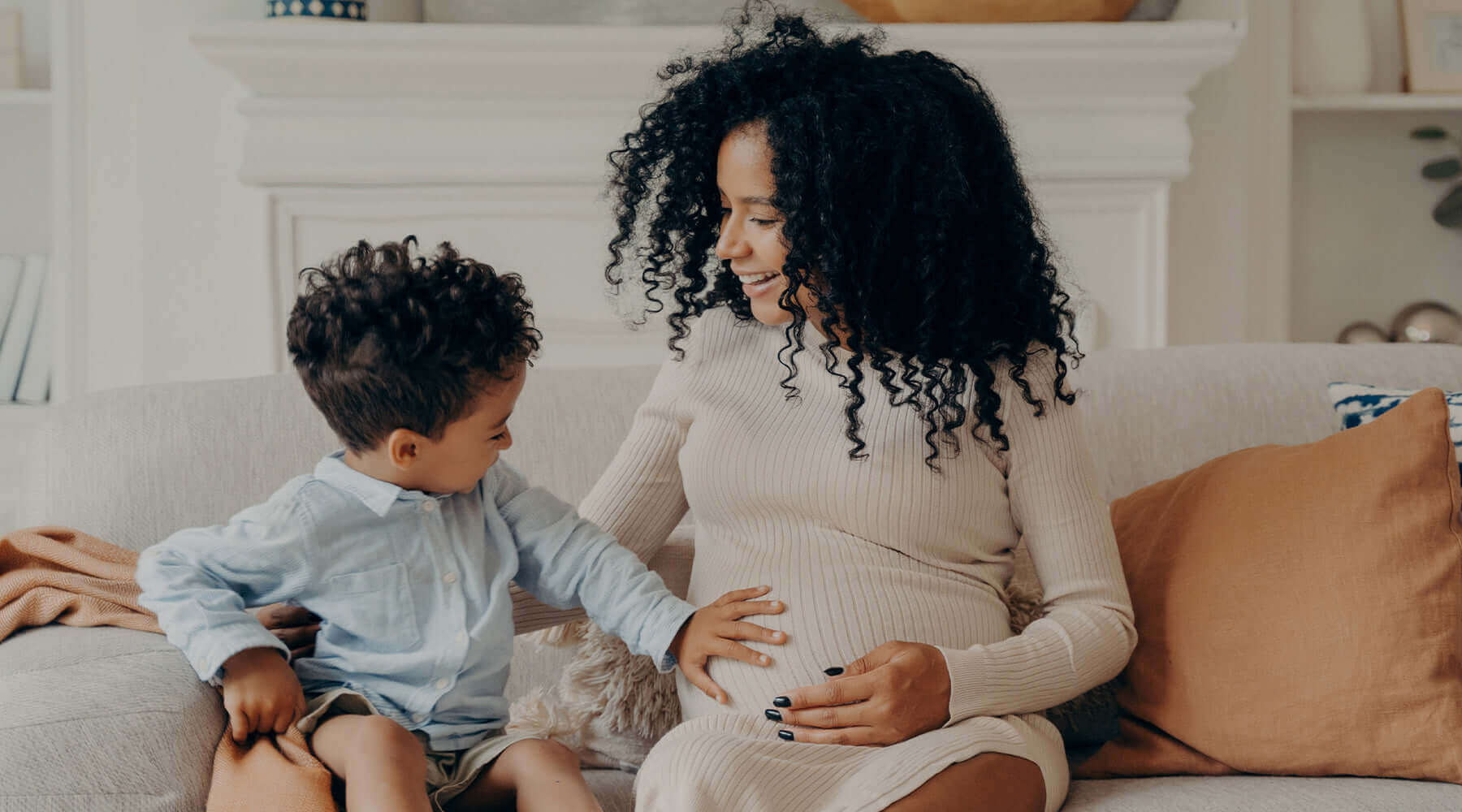Omega-3 During Pregnancy: Pregnant mom sitting on couch with child while child has hand on mom's stomach