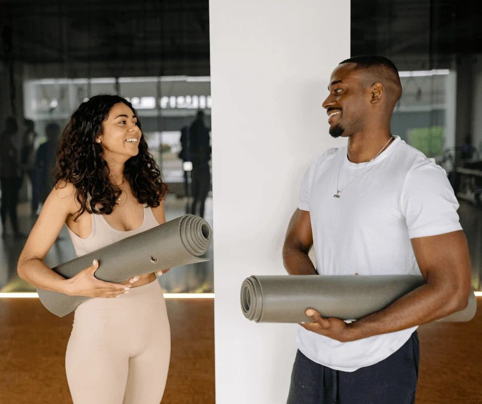 A man and woman smiling while holding yoga mats, reflecting wellness and fitness routines.