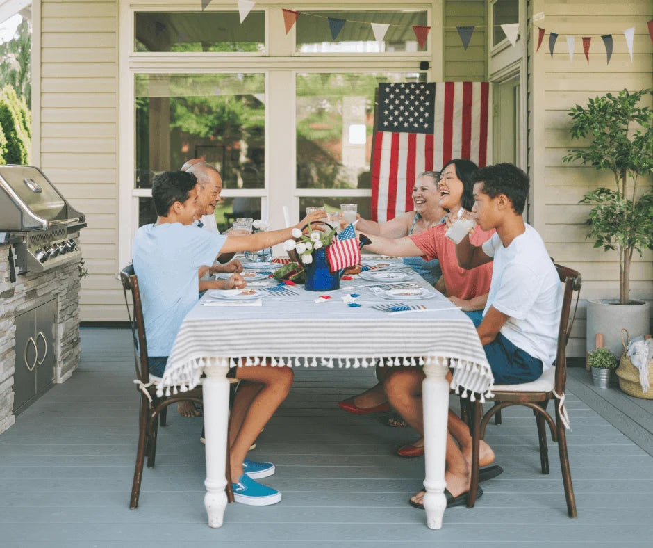 Family gathering around a festive table to celebrate with food and drinks for 5 Easy Ways to Add More Nutrition to Your 4th of July Spread.