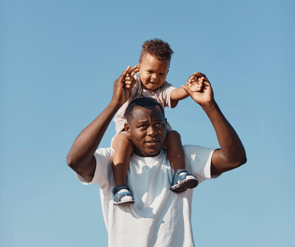 father holding son on his shoulders outside against a blue sky