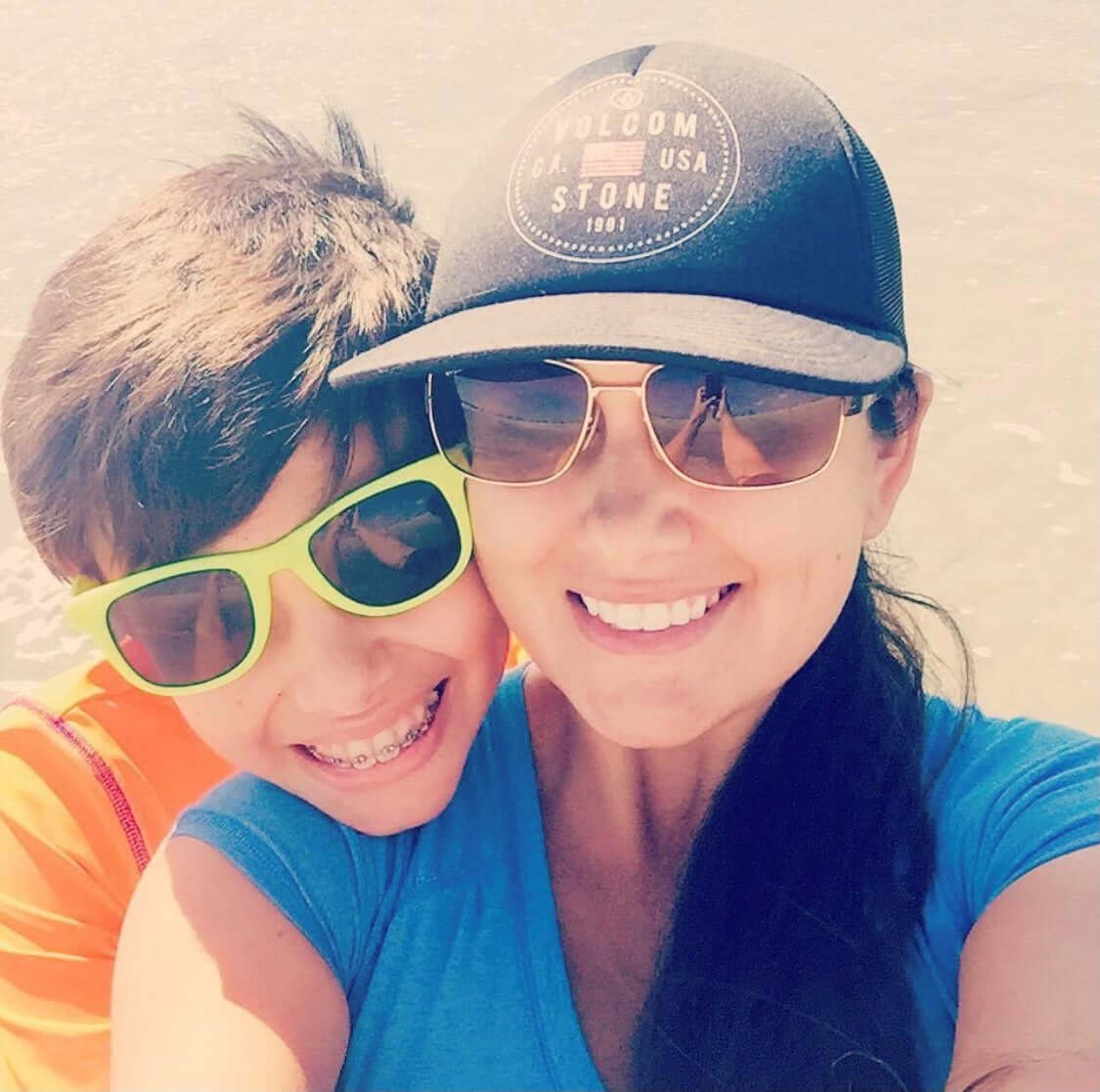 son with his head over his mother's shoulder wearing sunglasses and smiling