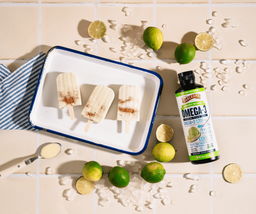 barlean's key lime pie fish oil on a tan colored countertop next to limes and popsicles and limes