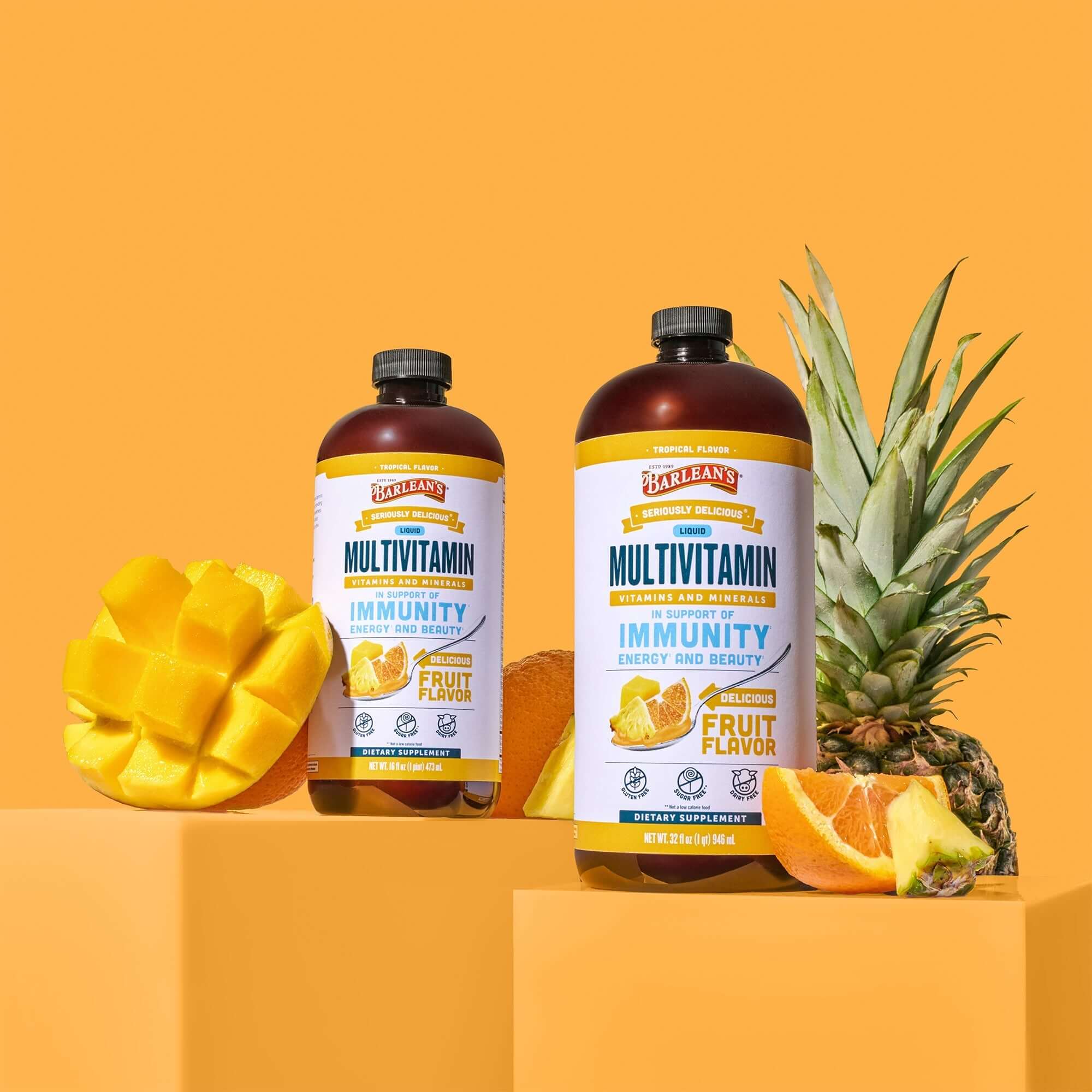 studio image of Barlean's tropical liquid multivitamin next to mangos, oranges, and pineapple, for immune health, energy, antioxidant support and overall wellness