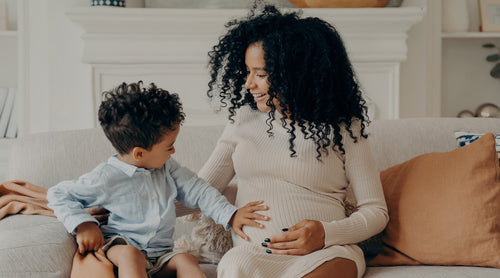 Image: Pregnant mom sitting on couch with child while child has hand on mom's stomach