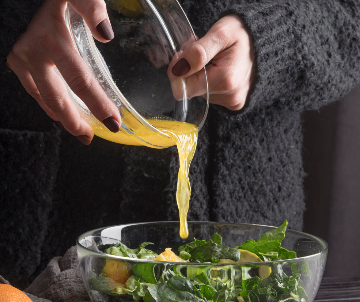 a glass bowl of Maple Dijon Harvest Vinaigrette dressing make with Barlean's organic fresh flax oil dressing getting drizzled over a bowl of greens
