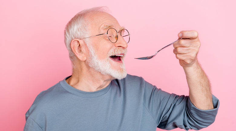 Image: Older man about to eat off of spoon in front of pink background