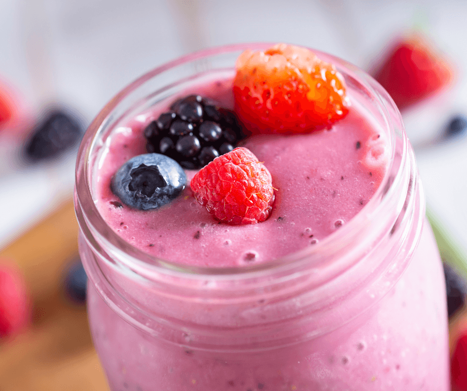 a bright pink smoothie in a glass mason jar with fresh berries on top