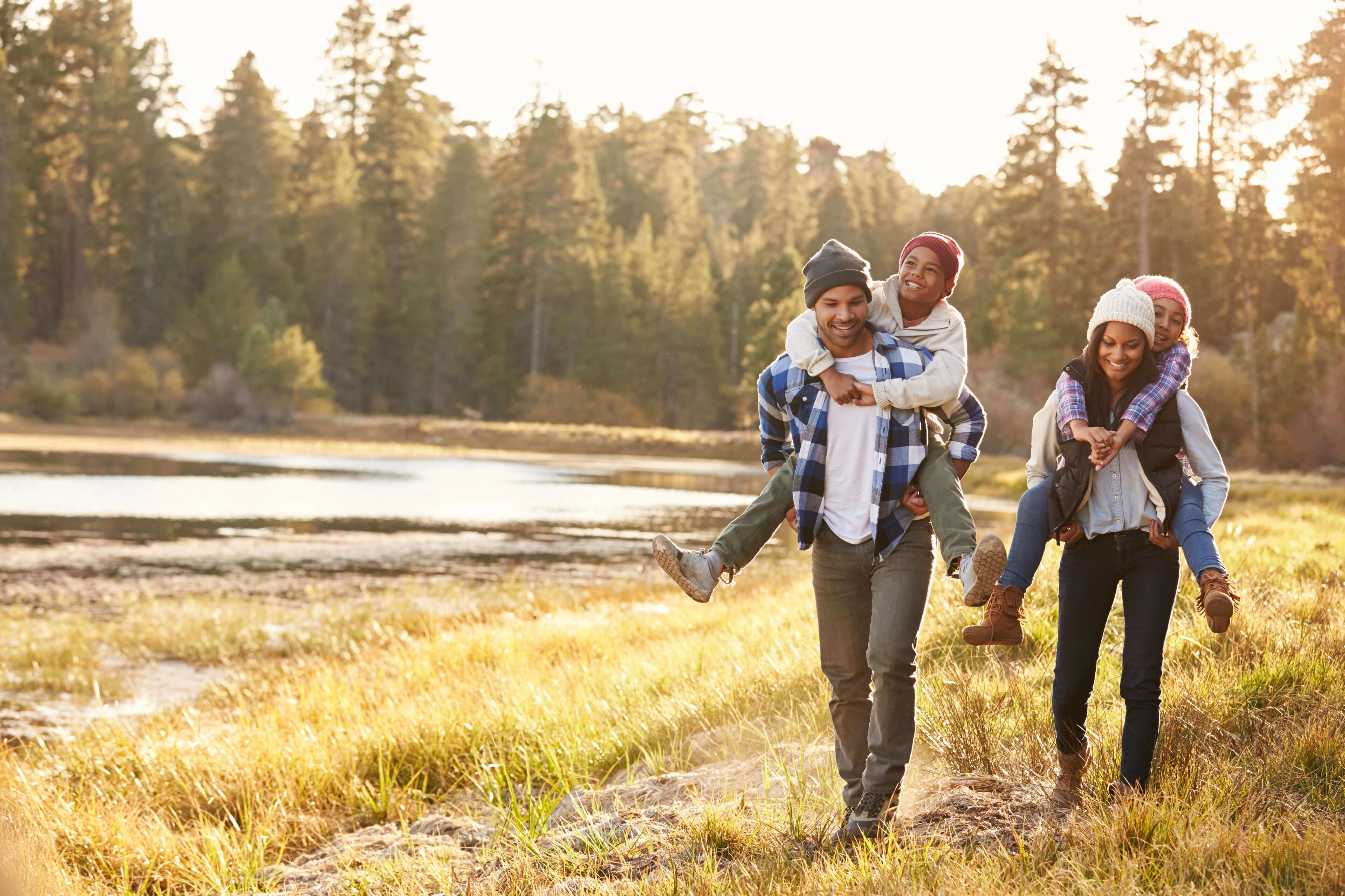 stress awareness month with a family walking outdoors with kids piggybacking on parents at sunset