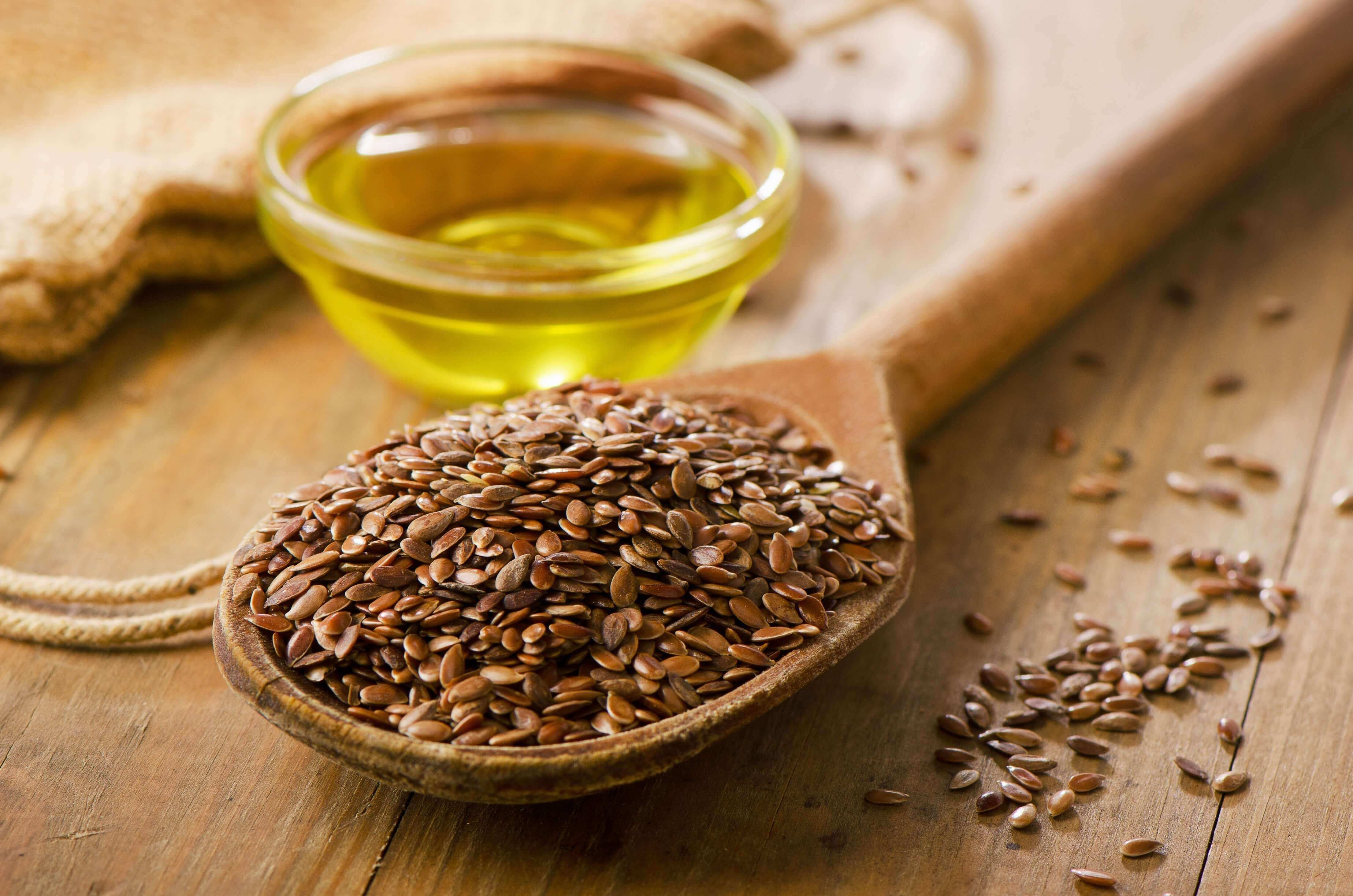 flaxseed on a spoon with flax oil in the background