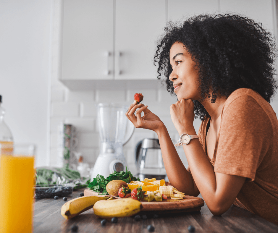 a woman in her kitchen eating fruits and vegetables laid out on the counter