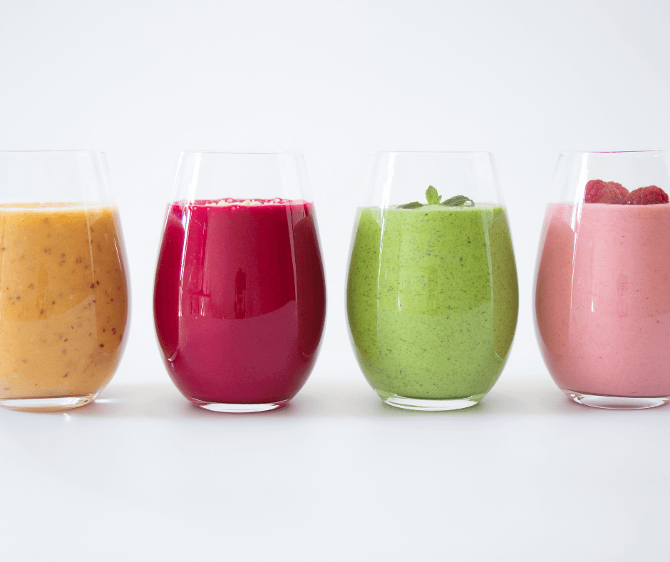 4 different colored smoothies (orange, red, green and pink) lined up in a row against a white background