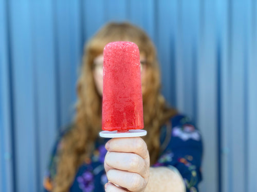 Woman holding up red popsicle.