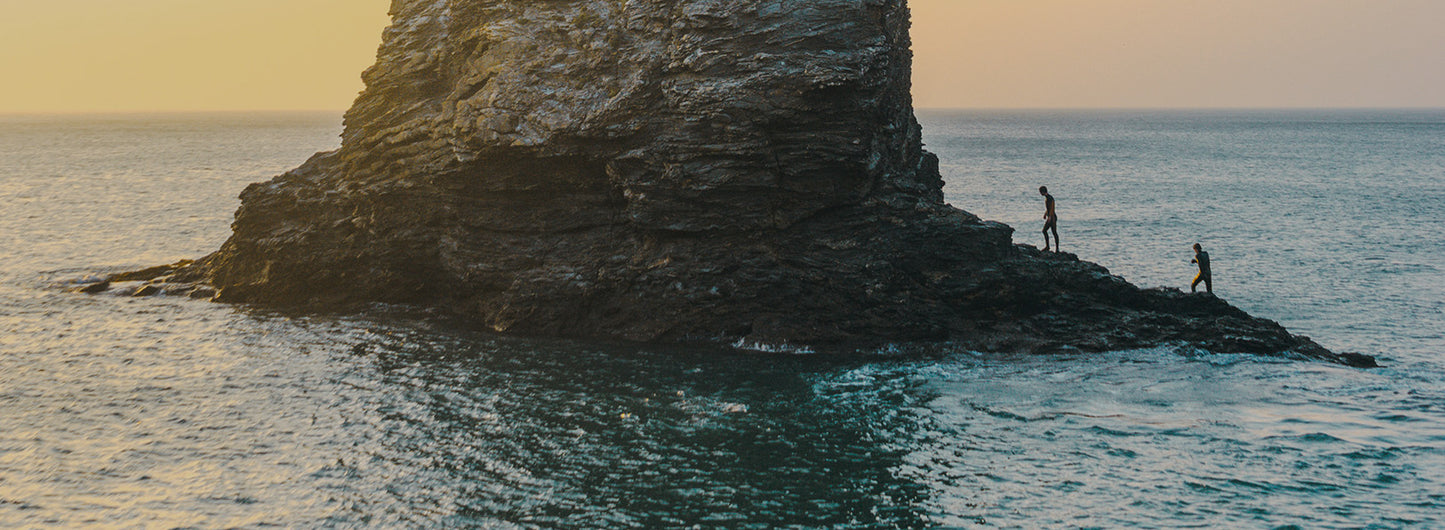 People walking on a rocky island in the water.